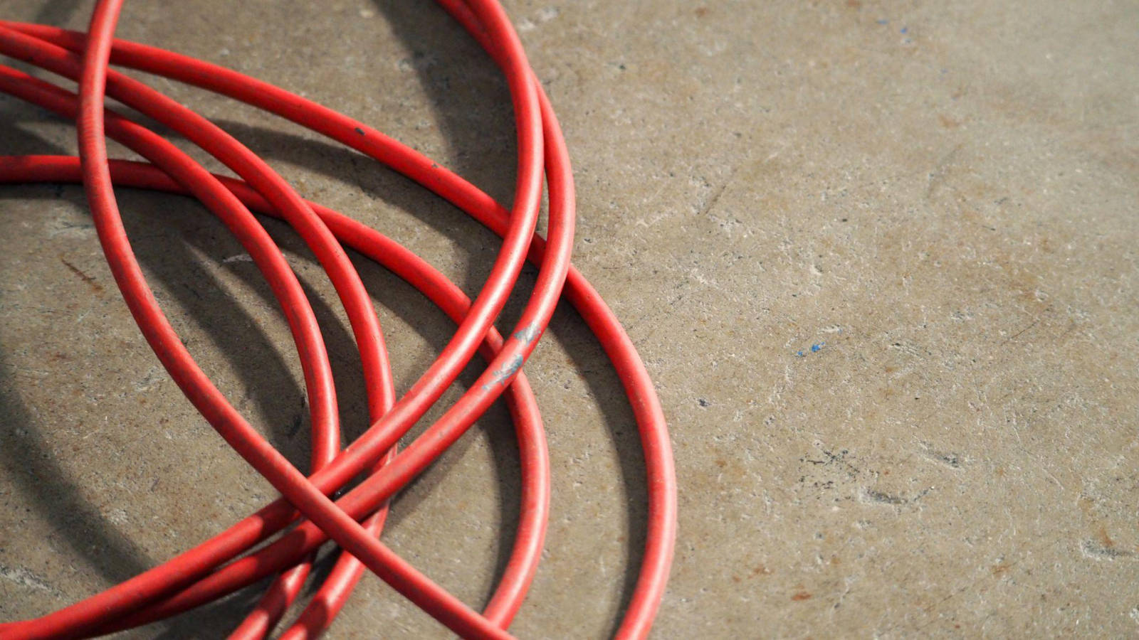 A red heavy-duty extension cord coiled on a concrete floor highlighting potential clutter and safety hazards without a proper distribution panel.