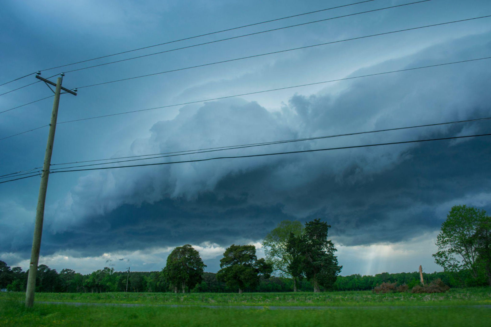 Dark storm clouds looming over power lines and utility poles in a rural landscape.