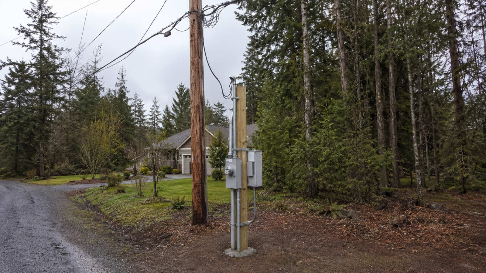 A newly installed wooden post set in concrete holding customer-owned electrical equipment next to a utility pole.