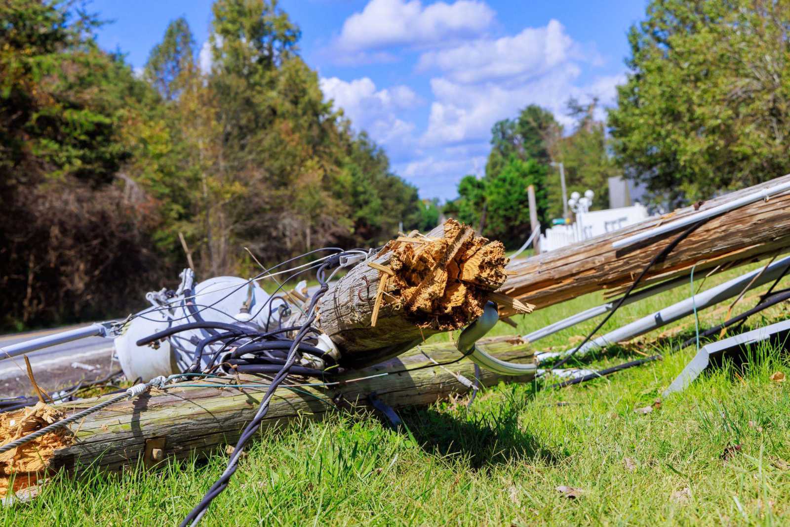 Close-up of a broken, splintered wooden utility pole lying on the ground with tangled power lines after severe storm damage.