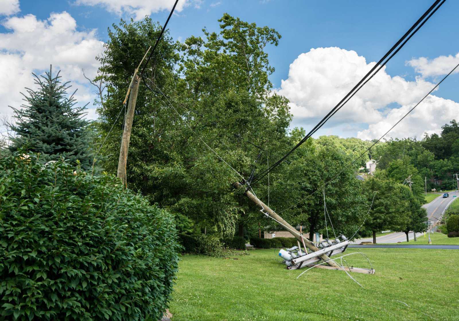 storm-damage-to-electrical-utility-pole A utility pole snapped and leaning severely into a grassy lawn following storm damage to electrical lines.