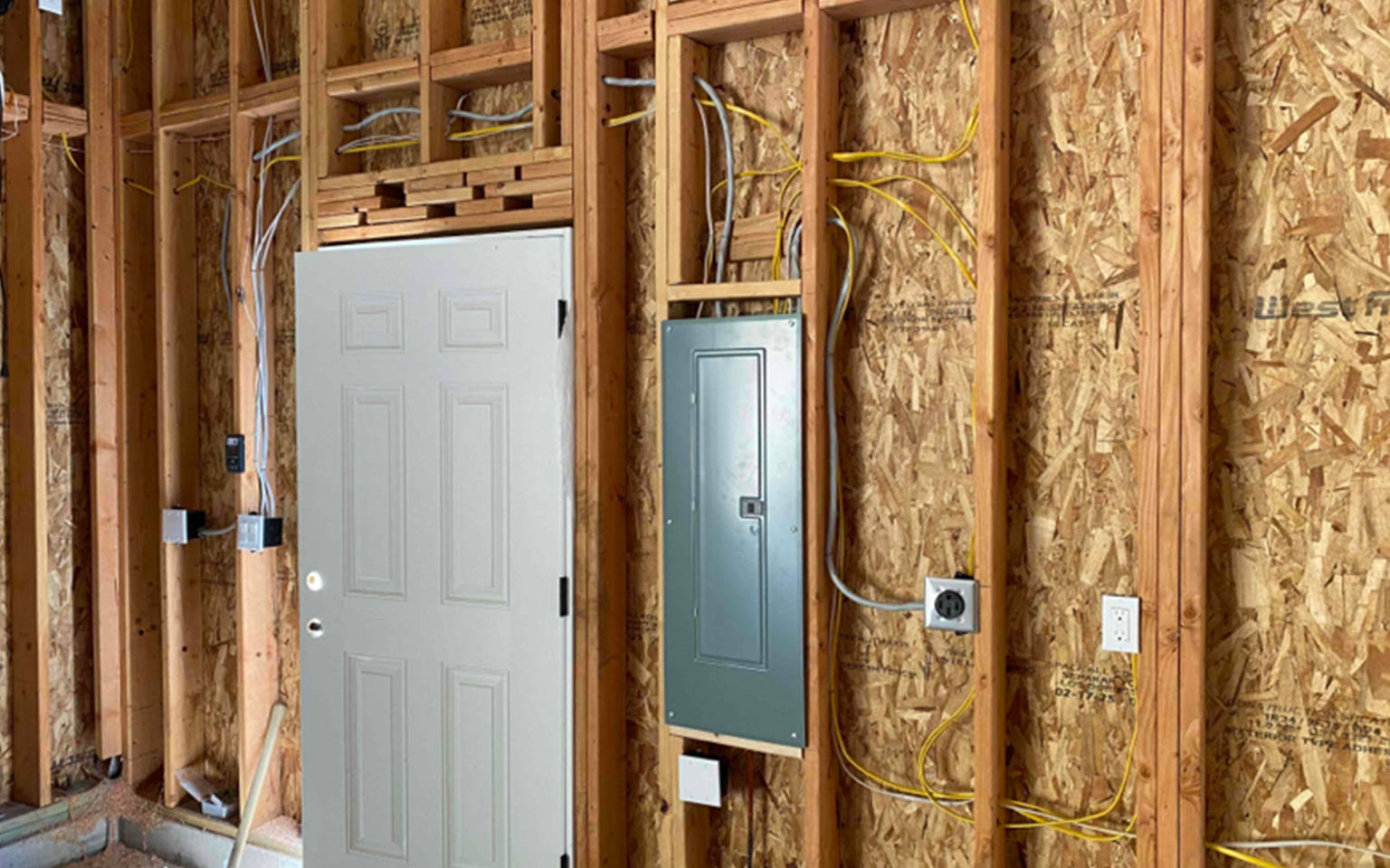 Newly installed electrical panel and fresh circuit wiring inside open wall framing during a home rewiring project.