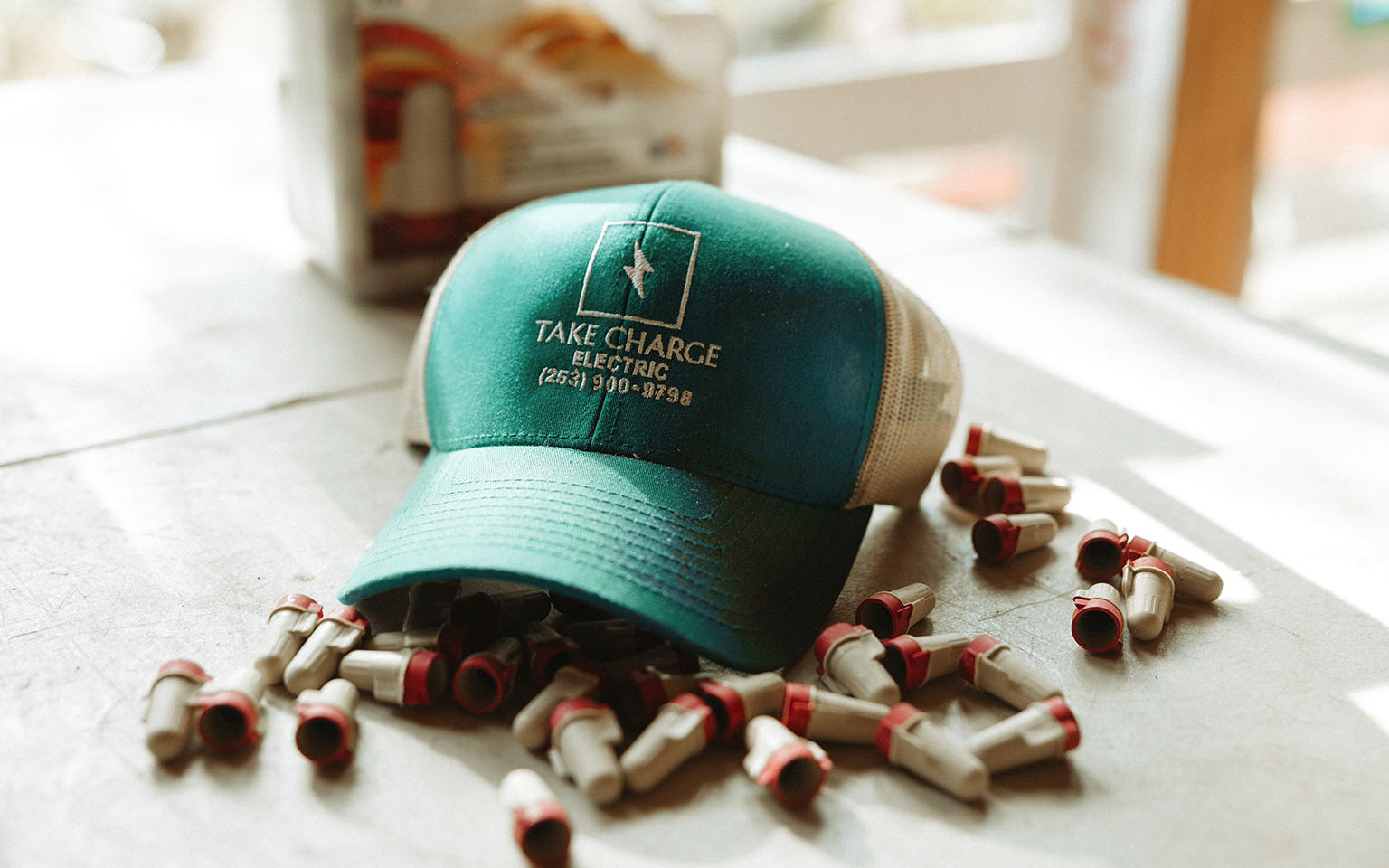 A teal Take Charge Electric hat sitting on a workbench surrounded by electrical wire connectors.